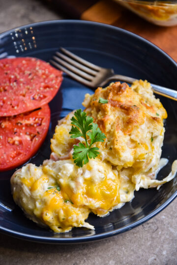 Plated serving of chicken bacon ranch casserole with two biscuits and a side of tomato slices.