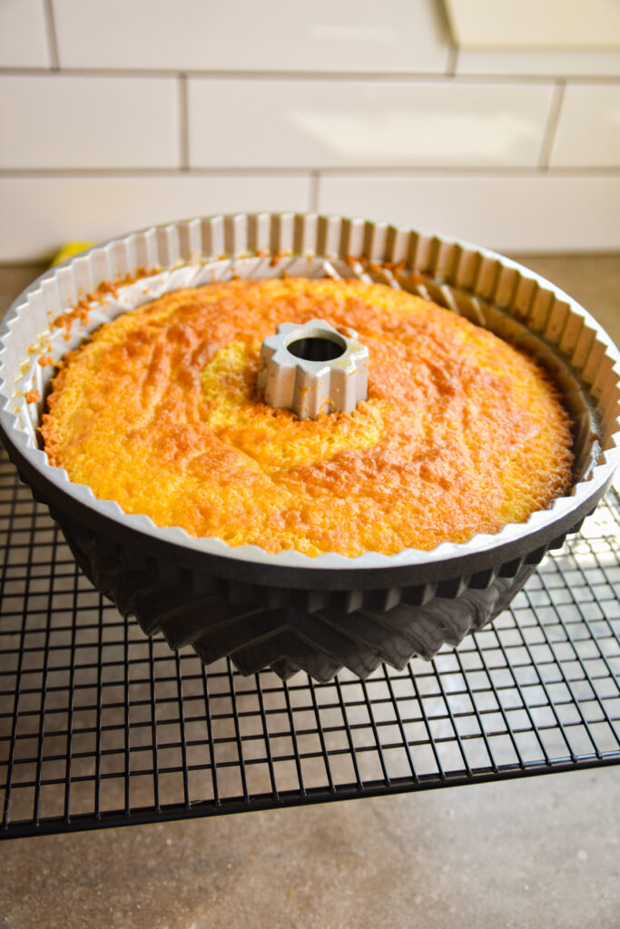 Baked lemon jello cake cooling in bundt pan on rack.