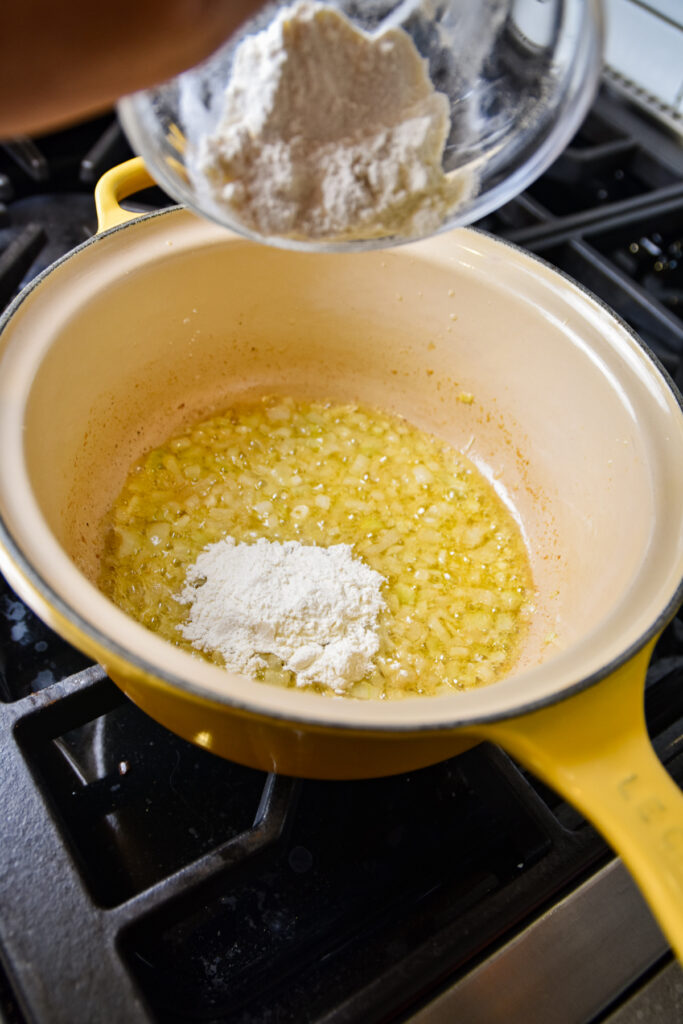 Adding flour to butter and onions to make a rue.