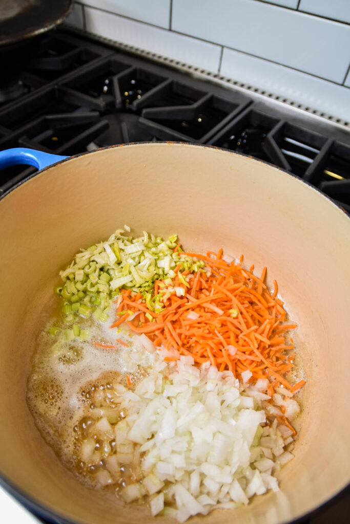 Dutch oven with onions, carrot, and celery cooking in butter.