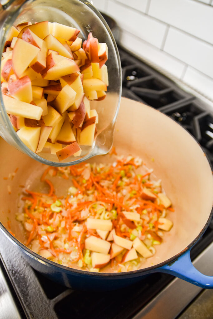Adding potatoes to sauted vegetables in a dutch oven.