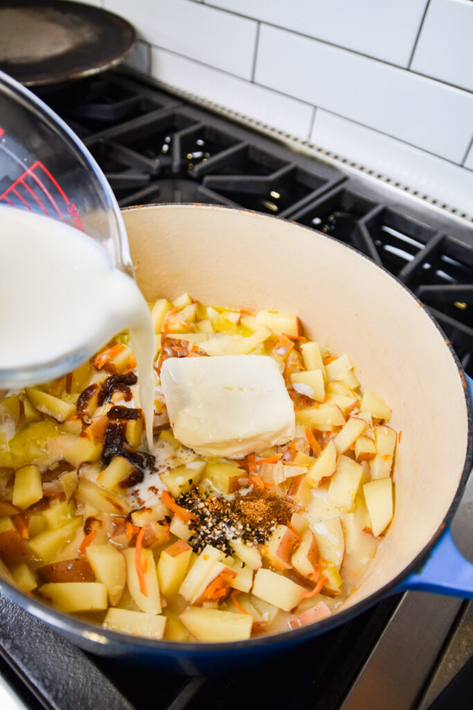Adding dairy to cooked potatoes for cheesy ham and potato soup.