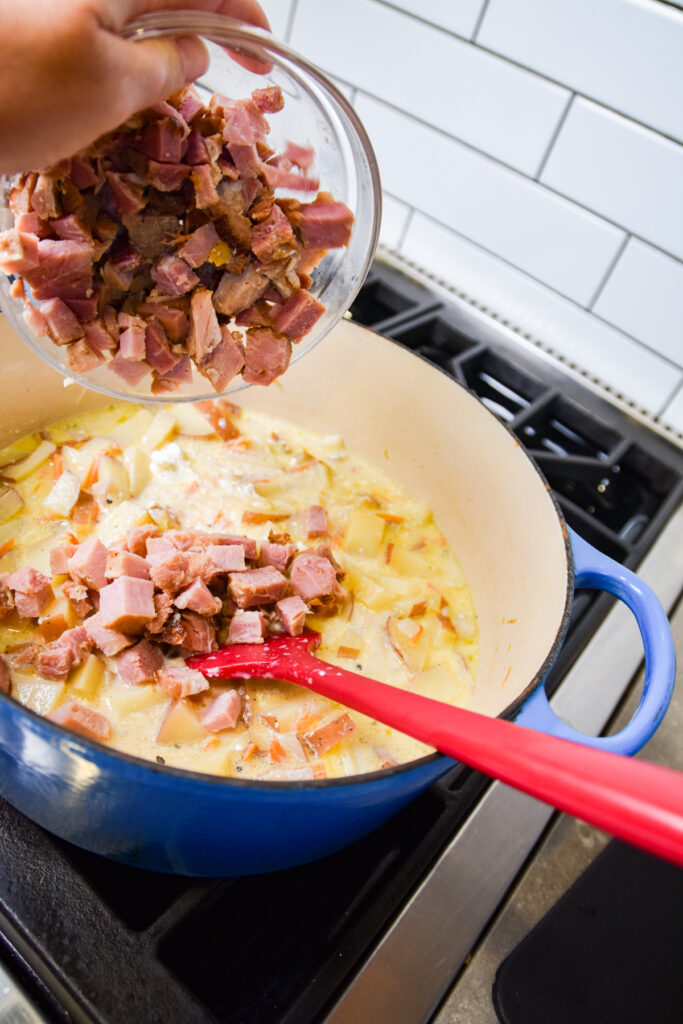 Adding cubed ham to cooked potatoes for soup.