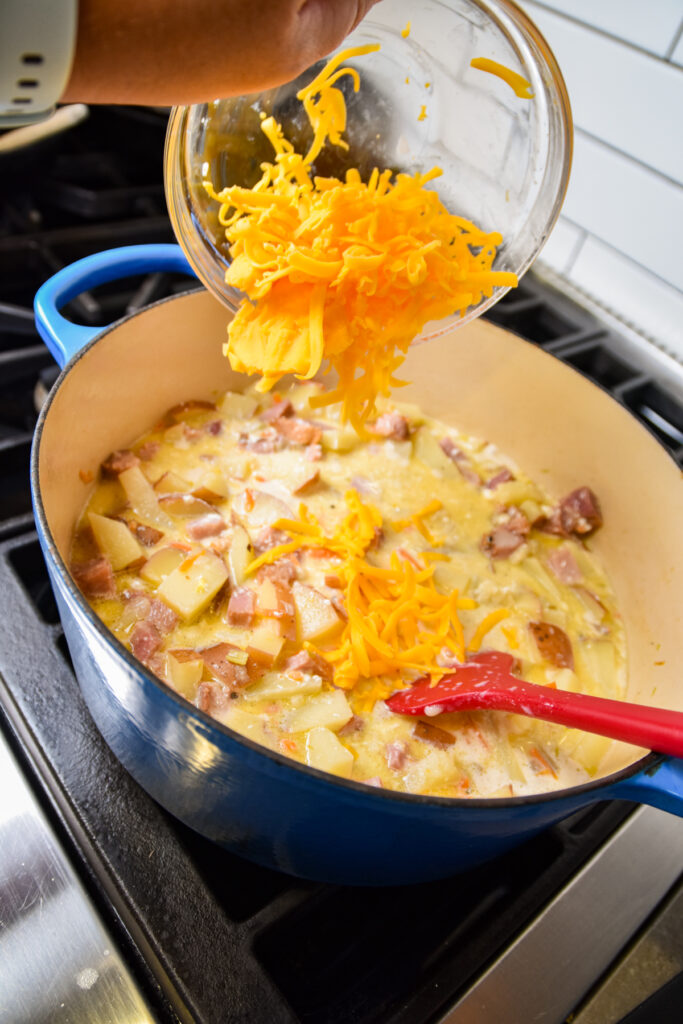 Adding shredded cheese to pot of potato soup with ham.