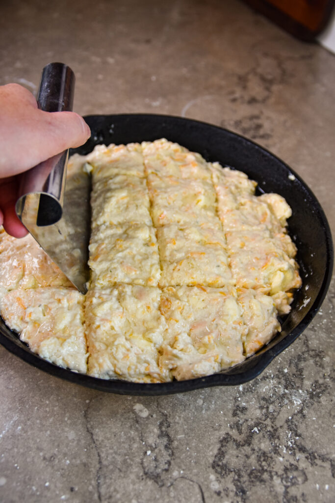 Cutting biscuits in a black iron skillet with a pastry scraper.
