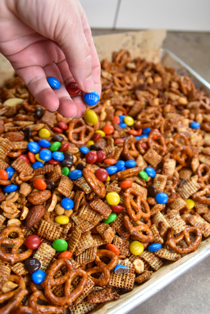 Sprinkling M&M candies over Crunchy Sorghum Snack Mix