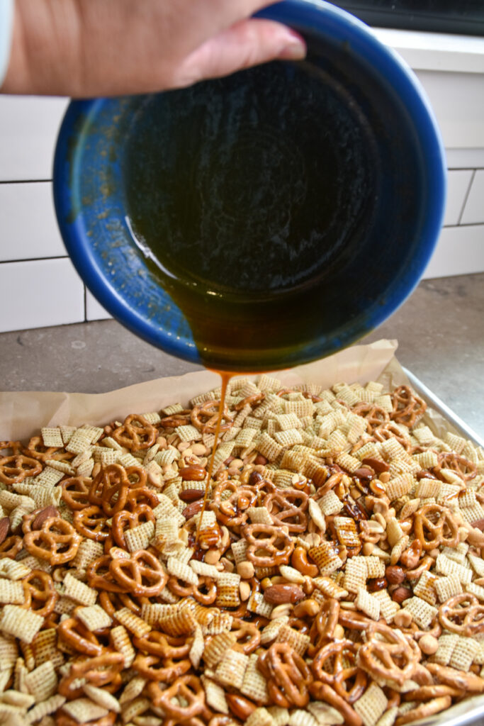 Adding melted butter, sorghum syrup, and vanilla to snack mix