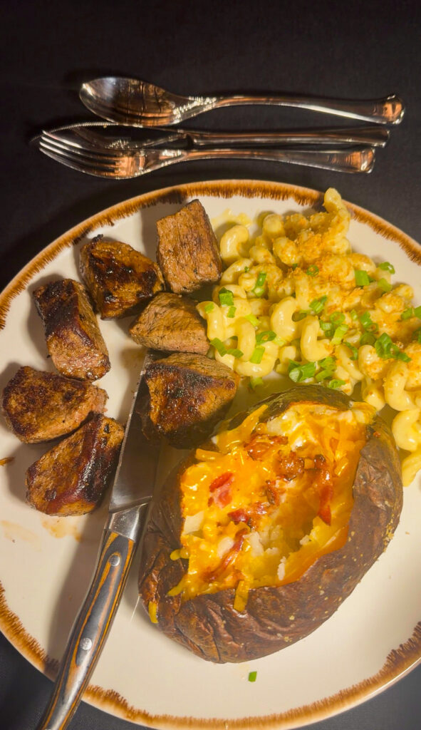 Beef tips with macaroni and cheese, with baked potato on a plate.